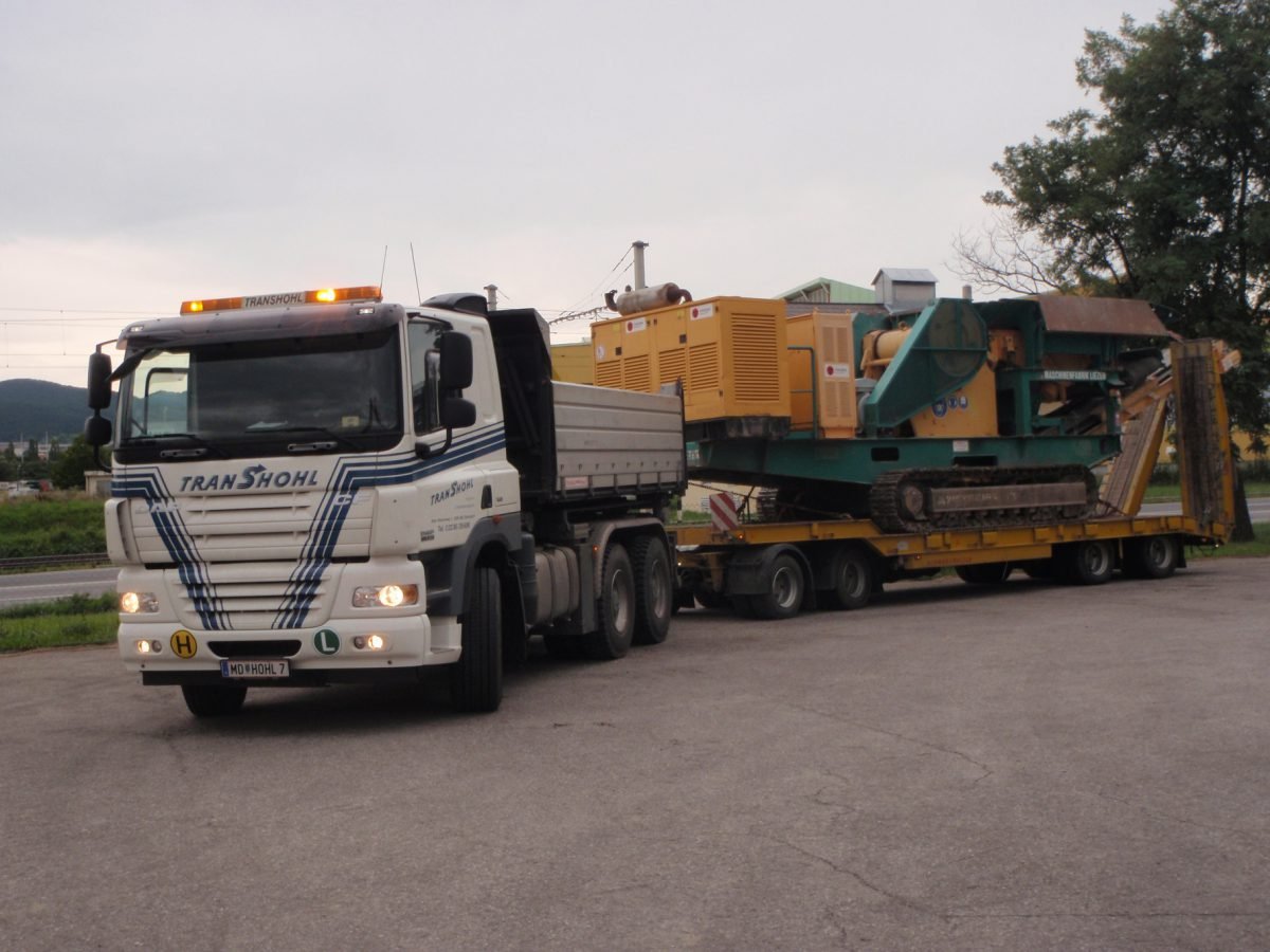 Trans-Hohl Tieflader mit transportierter Baumaschine